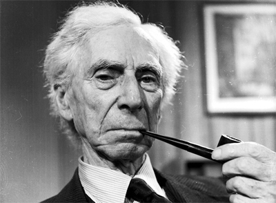 Black-and-white portrait of an elderly man with white hair holding a pipe to his mouth and looking at the camera indoors.