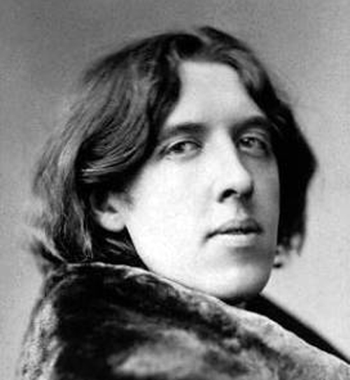 Black-and-white studio portrait of a 19th-century writer with shoulder-length wavy hair, wearing a fur-collared coat, head slightly turned and looking toward the camera.
